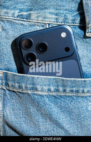 A sleek, modern smartphone with a triple-camera setup peeks out from a blue denim pocket. The close-up image highlights the phone’s design and advance Stock Photo