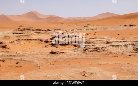 Breathtaking view of Deadvlei's desert landscape in Namibia, showcasing rugged terrain and striking orange sand dunes under a clear blue sky, offering Stock Photo