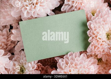 A soft green card lies nestled among delicate pink flowers, creating a romantic and elegant setting. Ideal for Valentine's Day greetings, love notes, Stock Photo
