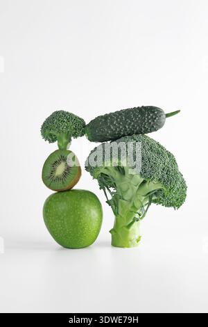 A vibrant arrangement of fresh organic fruits and vegetables, including kiwi, apple, cucumber, and broccoli, creatively stacked to showcase natural ba Stock Photo