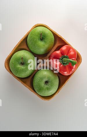 A top-down view of an eco-friendly cardboard tray holding three organic green apples and a vibrant red pepper, showcasing fresh, sustainable, and colo Stock Photo