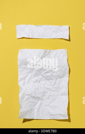 A close-up of two crumpled white paper sheets placed on a vivid yellow background, creating a contrasting and minimalistic composition that emphasizes Stock Photo