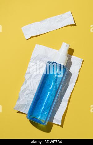A sleek blue spray bottle on crumpled white paper set against a vibrant yellow background, capturing the essence of modern cosmetic packaging with a f Stock Photo