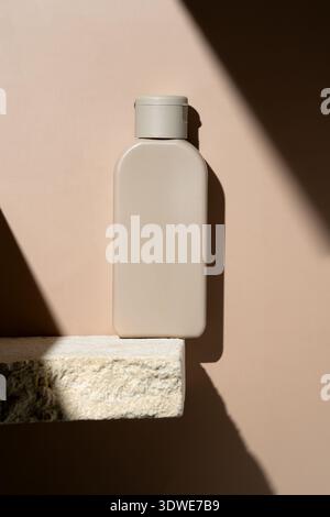 A sleek beige cosmetic bottle is elegantly placed on a textured stone shelf, beautifully illuminated by natural light. Ideal for showcasing minimalist Stock Photo