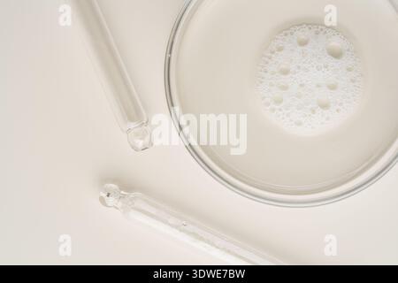 A top view of clear cosmetic product in a petri dish alongside droppers on a beige background. This image is ideal for showcasing skincare sciences an Stock Photo