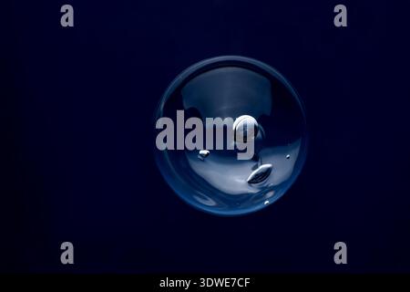 A clear bubble floating against a deep blue background, reflecting light with a smooth, glossy texture. It evokes a sense of calm and purity, resembli Stock Photo