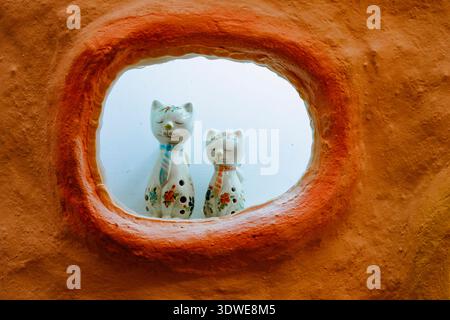 Ceramic cat figurines with floral designs are showcased in a rustic, clay-framed window in Taiwan. The playful decor adds a whimsical touch to the cul Stock Photo