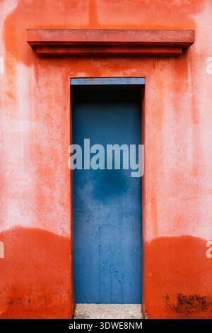 A striking blue wooden door set in a vivid red textured wall captures the essence of urban architecture in Taiwan, Asia. The colors create a dynamic v Stock Photo