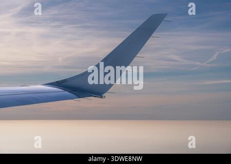 A tranquil scene of an airplane wing slicing through the sky during a serene flight over Taiwan. The soft sunset hues create a peaceful and expansive Stock Photo