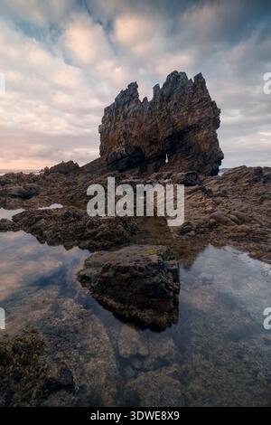 Rugged beauty of Playa Portizuelo in Asturias, Spain. The cloudy summer sky casts a dramatic backdrop over the unique rock formations and tranquil sea Stock Photo