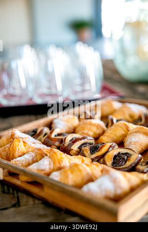 A close-up of assorted pastries on a wooden tray in a restaurant setting. The blurred background showcases empty glasses, creating a warm and inviting Stock Photo