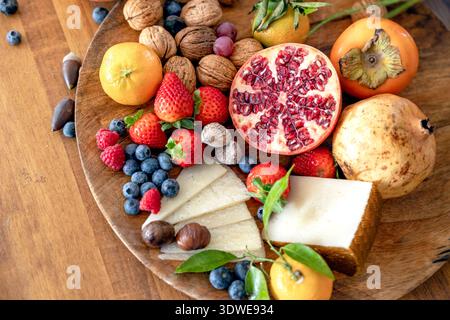 A delightful assortment of fresh fruits including strawberries, blueberries, tangerines, figs, and cheese displayed on a rustic wooden board, perfect Stock Photo