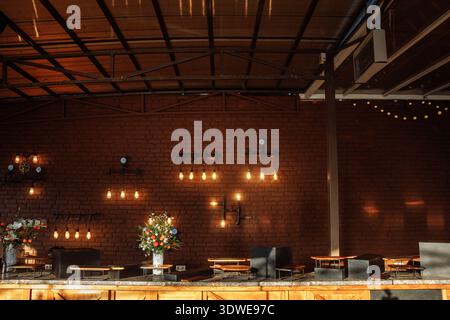 Warmly lit outdoor cafe with exposed brick wall, vintage hanging bulbs, and floral arrangements, ideal for restaurant promotions and interior design p Stock Photo