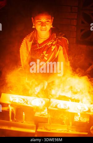 Sonargaon, Bangladesh - 15 November 2022: View of a woman's face illuminated by the fiery glow of candles, casting a warm, ethereal light against the Stock Photo