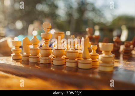 A beautifully crafted set of wooden chess pieces arranged on a vintage board, illuminated by warm sunlight, capturing the essence of medieval elegance Stock Photo
