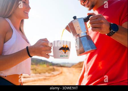 A young couple cherishes freshly brewed coffee from a nature-themed mug while hiking in the scenic Red Canyon in Spain, embracing outdoor exploration Stock Photo