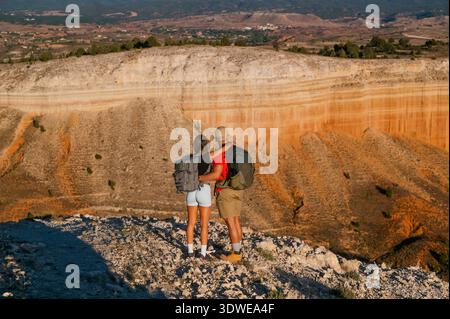 Back view of a couple embracing at the edge of Red Canyon in Spain, wearing hiking gear and enjoying the natural landscape and layered rock formations Stock Photo