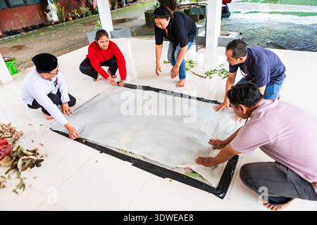 Group of people working together to cover a large cloth with leaves, an essential part of the traditional Indonesian batik-making process using natura Stock Photo