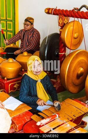 An elderly woman and a man perform in a traditional Javanese gamelan ensemble, showcasing cultural heritage with gongs and metallophones in a vibrant Stock Photo