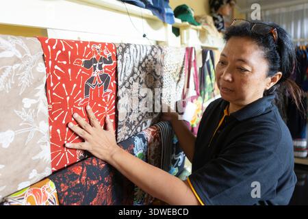 A woman inspects colorful batik fabrics, showcasing intricate patterns typical of traditional textile design, in a vibrant shop. Perfect for exploring Stock Photo