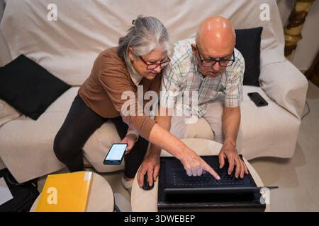 Elderly couple using a laptop and smartphone together, exemplifying digital inclusion. They represent active seniors managing financial wellbeing in t Stock Photo