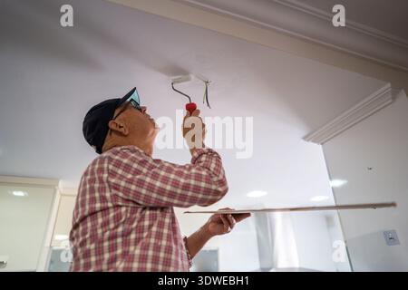 An active senior working on a DIY kitchen renovation, painting the ceiling with a roller brush. The scene captures the essence of creativity and hands Stock Photo