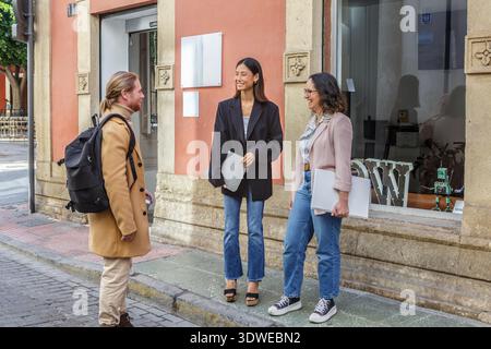 A diverse group of young professionals meets casually outside a modern coworking office, showcasing collaboration and discussion in a relaxed business Stock Photo