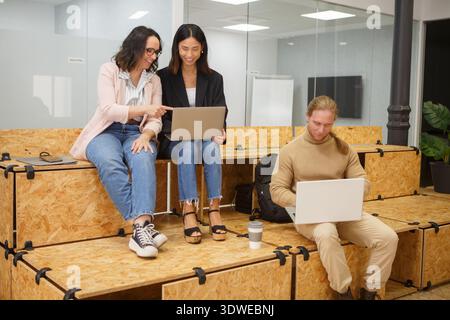 A diverse group of professionals engaged in a casual meeting at a coworking space, collaborating with laptops, discussing ideas, and working on a star Stock Photo