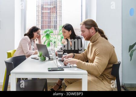 A diverse group of professionals engaged in a collaborative meeting at a coworking space. They are working on laptops, discussing business strategies Stock Photo