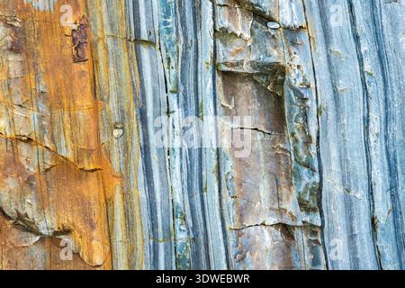 Close up of a multicolor sea rock displaying intricate patterns and a blend of blue, gray, and rust hues. The natural cracks and textures add depth to Stock Photo
