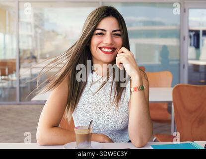 Smiling woman taking a break while telecommuting from a cafe. She enjoys coffee, relaxing during a busy workday, showcasing a modern lifestyle and fle Stock Photo
