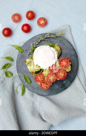 A nutritious breakfast plate featuring a poached egg atop mashed avocado spread on toast, garnished with fresh cherry tomatoes and greens, offering a Stock Photo