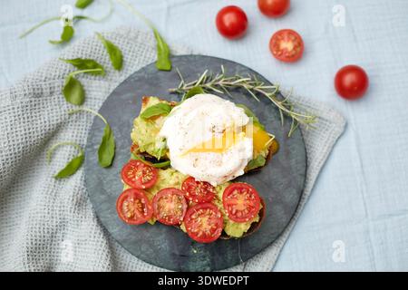 A nutritious breakfast of poached egg on toast with smashed avocado, cherry tomatoes, and fresh greens. Perfect for starting the day with a healthy, f Stock Photo