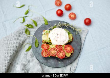 A delightful breakfast spread featuring avocado toast topped with a perfectly poached egg, fresh cherry tomatoes, and vibrant greens on a rustic stone Stock Photo