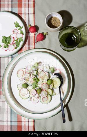 A refreshing salad featuring sliced radishes, cucumbers, and green grapes on a white plate. Garnished with parsley and a sprinkle of spices, set on a Stock Photo