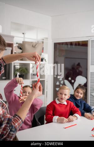 Children engaged in creating Christmas decorations using colorful plasticine. They are crafting candy cane ornaments, enhancing their creativity and f Stock Photo