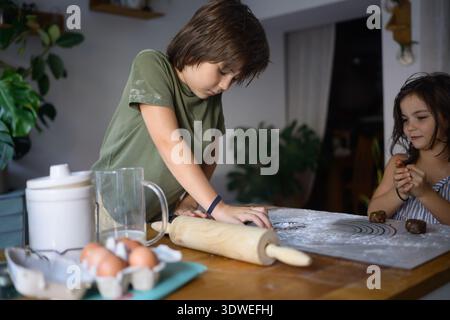 Two kids enjoy learning and baking together in the kitchen. They are making cookies, surrounded by ingredients and tools, capturing the essence of chi Stock Photo