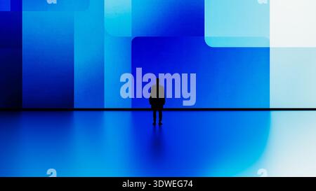 A man stands still in front of a large digital screen displaying blue geometric shapes. Stock Photo