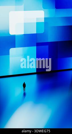 A man stands still in front of a large digital screen displaying blue geometric shapes. Stock Photo