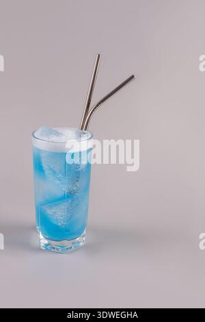 Refreshing blue matcha beverage served cold in a tall glass with ice cubes and two reusable metal straws, highlighting a modern and eco-friendly lifes Stock Photo