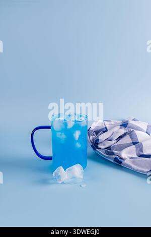 A vibrant blue matcha iced drink in a glass cup sits beside a checkered napkin on a light blue surface. The refreshing beverage is complemented by ice Stock Photo
