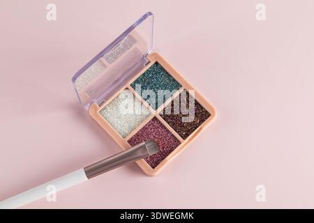 A vibrant eyeshadow palette featuring glittery shades in a pink compact case. Includes a brush for easy application. Perfect for creating decorative e Stock Photo