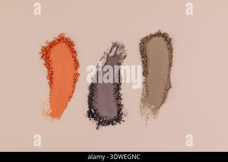 Three vibrant cosmetic powder swatches in orange, gray, and beige displayed artistically on a neutral background, representing beauty and texture in m Stock Photo
