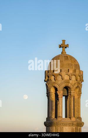 Stone tower at Tibidabo in Barcelona during sunset, with a full moon in the clear sky. The golden hour light enhances the architectural details agains Stock Photo