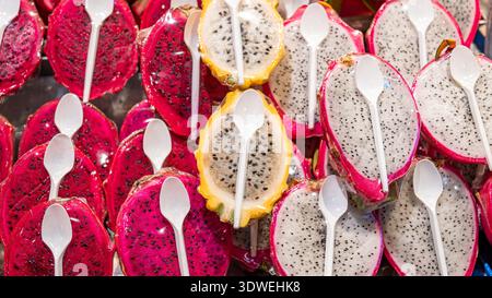 Vibrant dragon fruit halves on display, featuring a vivid pattern of red and yellow skin with black seeds. Each fruit slice is paired with a white pla Stock Photo