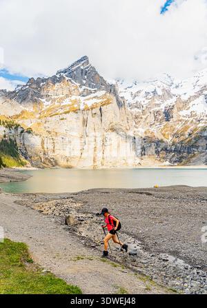 A hiker explores the breathtaking landscape of Oeschinen Lake in the Swiss Alps during spring. Surrounding scenery includes majestic mountains and a s Stock Photo