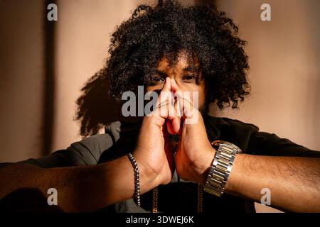 Studio portrait of a man with an afro hairstyle. He appears pensive, his hands thoughtfully clasped in front of his face, while soft lighting adds dep Stock Photo
