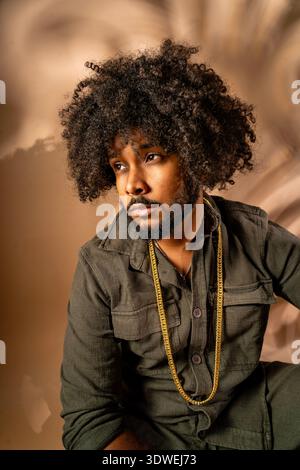 Portrait of a man with an afro hairstyle, adorned in a fashionable outfit, posing thoughtfully in a studio. The background is softly blurred, enhancin Stock Photo