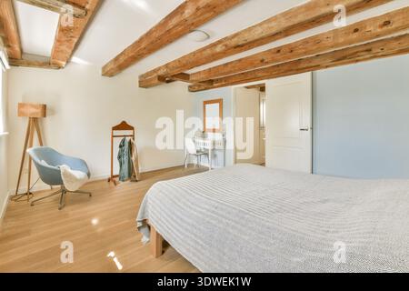 A stylish bedroom showcasing wooden ceiling beams, cozy seating, and modern decor. The combination of textures and colors creates a relaxing atmospher Stock Photo
