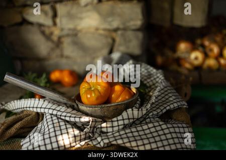 A rustic kitchen scene with organic seasonal tomatoes in an antique metal container, placed on a checkered cloth. The natural light accentuates their Stock Photo